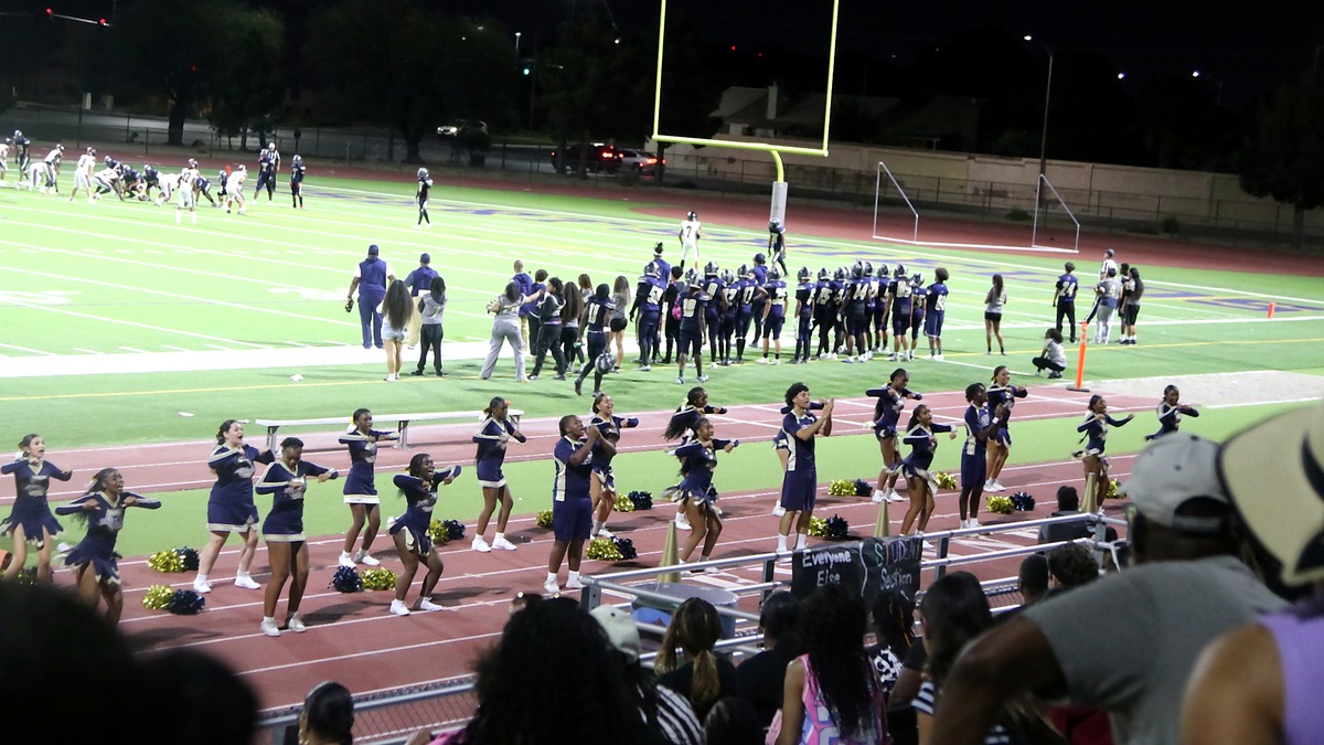 Cheyenne High School cheerleaders performing while the football team watches from the sideline